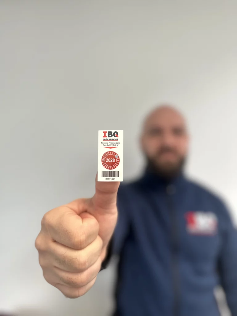 Qualifizierte Elektroprüfung durch IBQ mit dokumentiertem Prüfergebnis IBQ-Prüfer zeigt eine Prüfplakette für ein kontrolliertes elektrisches Betriebsmittel