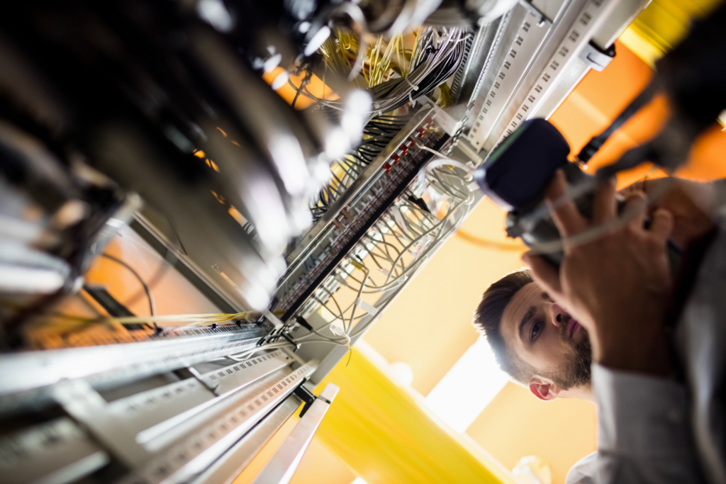 Techniker kontrolliert die Verkabelung in einem dicht bestückten Technikschrank
